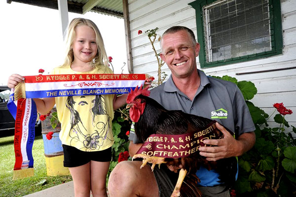 A man holding a rooster with a winners ribbon and a girl standing next to him holding another ribbon