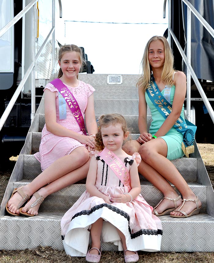 Three Showgirls wearing their sashes sitting on stairs